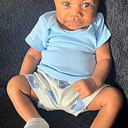 Zaiden is registered to the contest to win money with this photo: baby, infant, child, blue_shirt, shorts, socks, couch, furniture, seated, portrait, face, eyes, skin, expression, indoor, cute, person, young_child, sitting, clothing