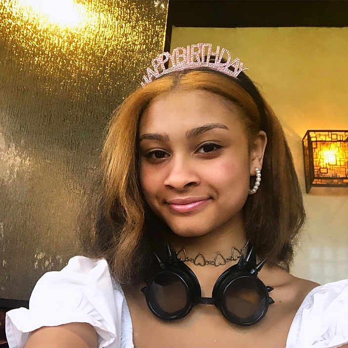 Sariyah Horn is registered to the contest to win money with this photo: accessories, birthday_tiara, casual, decor, earrings, face, fashion, female, goggles, hair, happy, head_and_shoulders, indoor, lamp, necklace, portrait, smiling, warm_lighting, white_clothing, young_person