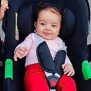 Talya a rejoint le concours — aidez-le/la à gagner de superbes lots ! baby, infant, stroller, child, smiling, red_pants, white_socks, hair_pigtails, car_seat, safety_harness, outdoor, sidewalk, cute, happy, person, small_hands, bright_clothing, seatbelt, playful, toddler