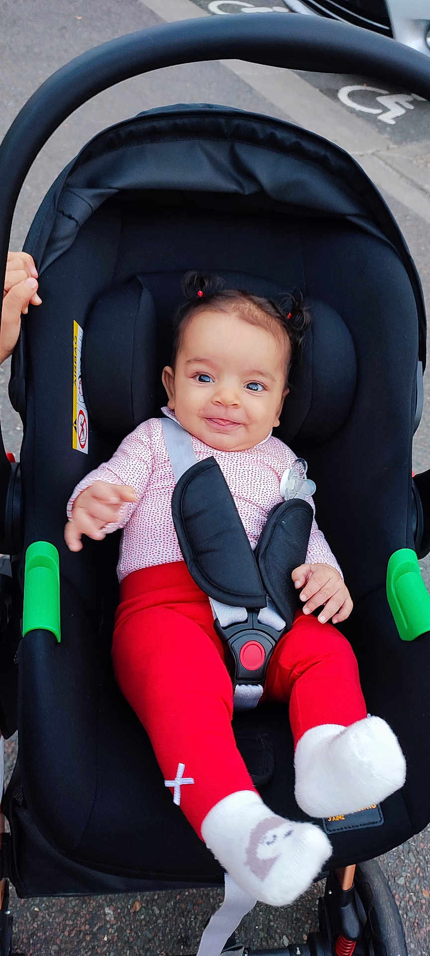 Talya a rejoint le concours — aidez-le/la à gagner de superbes lots ! baby, infant, stroller, child, smiling, red_pants, white_socks, hair_pigtails, car_seat, safety_harness, outdoor, sidewalk, cute, happy, person, small_hands, bright_clothing, seatbelt, playful, toddler