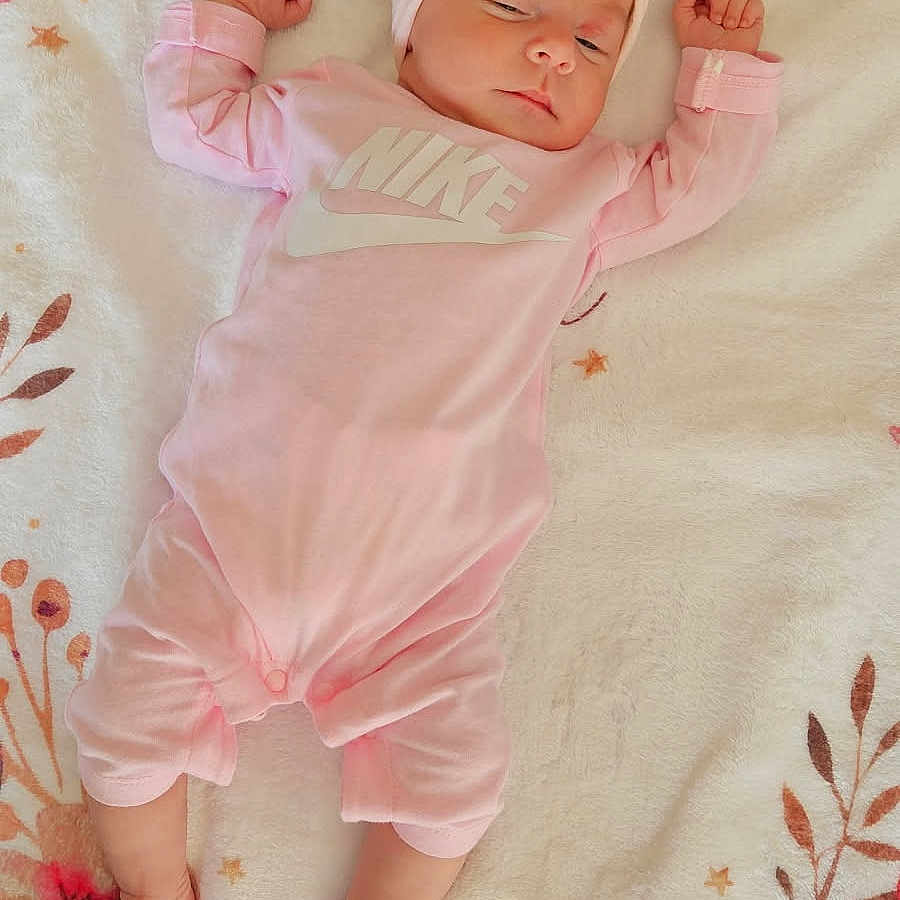 Romy participe au concours pour gagner de l'argent avec cette photo : arms_up, baby, blanket, comfortable, cute, face, floral_pattern, foot, hand, headband, indoors, infant, legs_stretched, newborn, person, pink_clothing, resting, sleeping, soft_texture, toddler