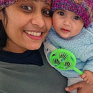 Nishitha is registered to the contest to win money with this photo: adult, baby, child, close_up, colorful_hat, cute, face, family, green_toy, hand, happy, holding, indoor, knitted_hat, person, portrait, smiling, sweater, toy, warm_clothing