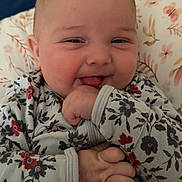 Octavia is registered to the contest to win money with this photo: baby, child, smiling, floral, onesie, hand, face, cushion, indoor, cute, infant, person, young, happy, cheeks, sitting, comfort, pattern, cozy, portrait