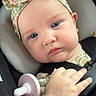 baby, infant, car_seat, headband, bow, pacifier, clothing, straps, hand, face, blue_eyes, expression, closeup, child, seatbelt, cute, skin, portrait, safety, floral_pattern