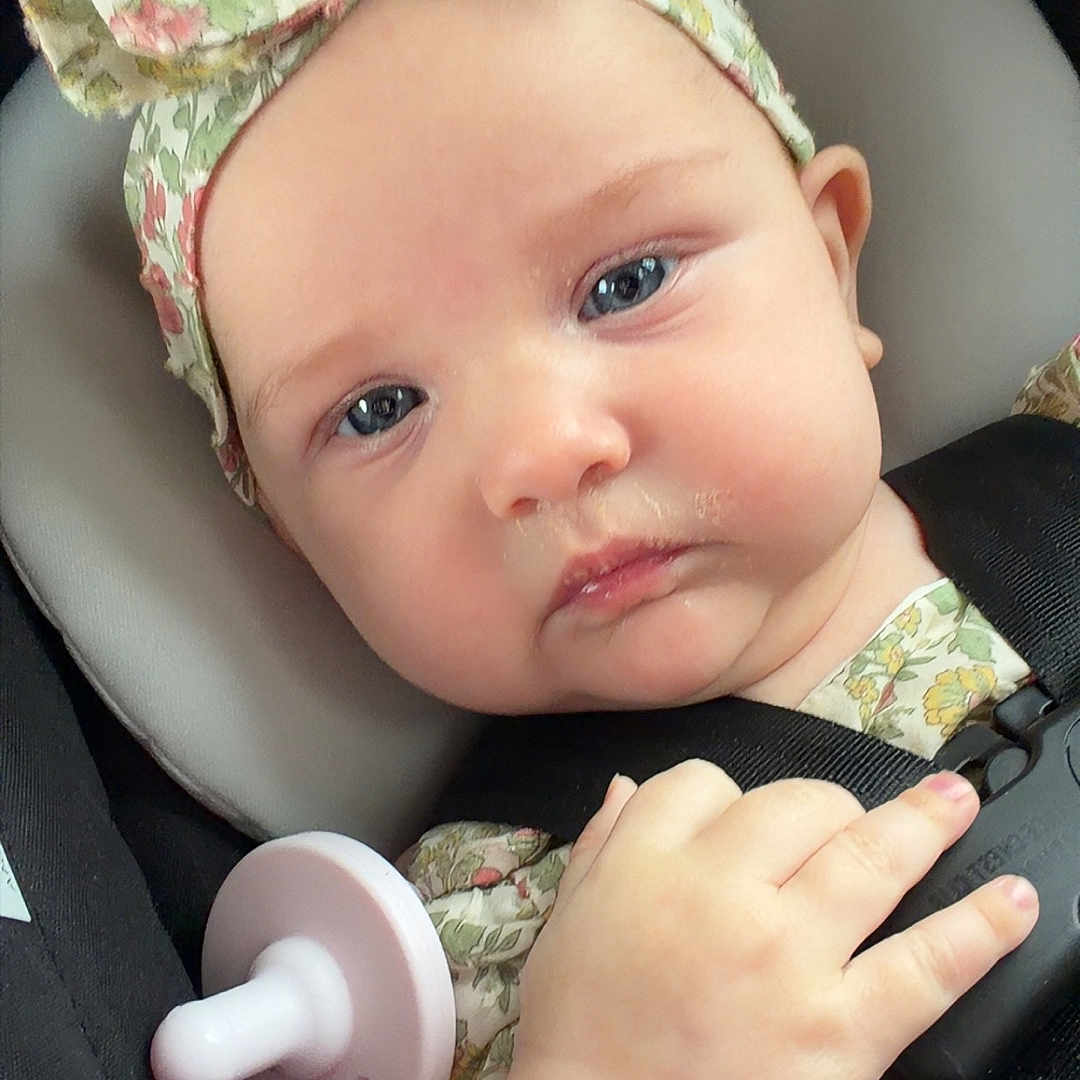 Octavia joined the competition — help win amazing prizes! baby, infant, car_seat, headband, bow, pacifier, clothing, straps, hand, face, blue_eyes, expression, closeup, child, seatbelt, cute, skin, portrait, safety, floral_pattern