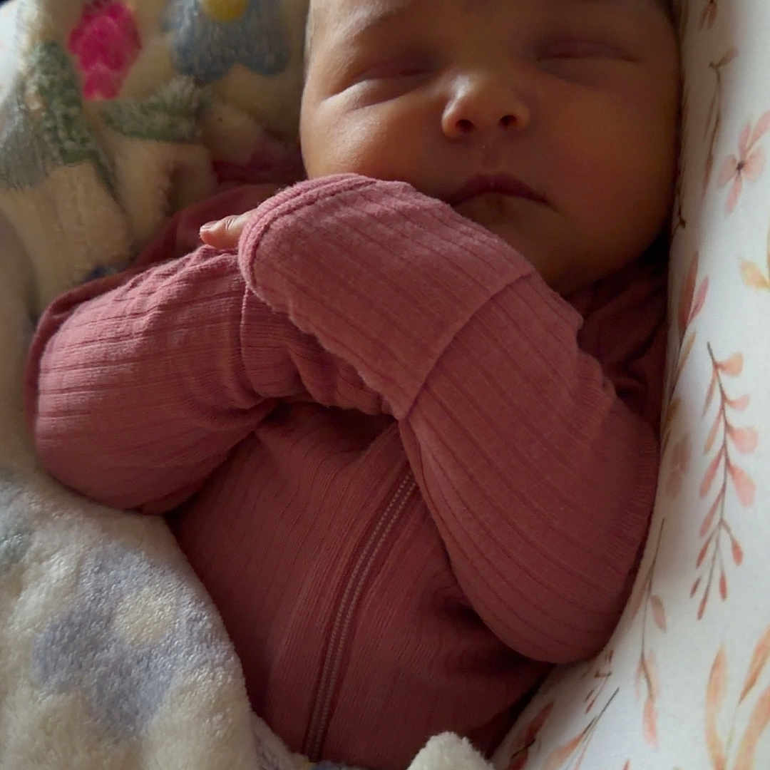 Octavia is registered to the contest to win money with this photo: baby, newborn, sleeping, blanket, pink_clothing, floral_pattern, cushion, infant, resting, cozy, soft_texture, child, portrait, indoors, peaceful, cute, wrapped, baby_girl, closeup, tender_moment