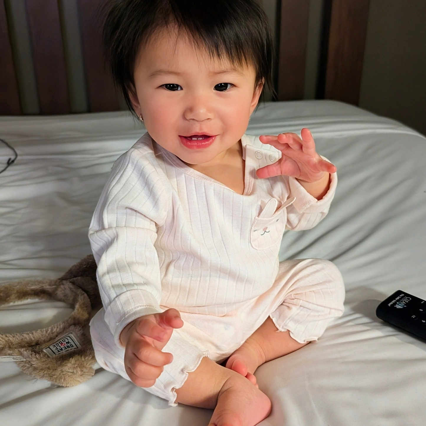 Natalie is registered to the contest to win money with this photo: toddler, child, baby, pajamas, bed, white_bed, smiling, happy, indoor, person, face, hair, hands, feet, remote_control, headband, cute, cozy, casual, portrait