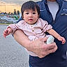 baby, child, person, adult, holding, outdoor, street, sky, cloudy, evening, jacket, pink_clothing, cute, portrait, hand, face, expression, casual, urban, family