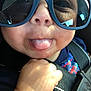 Isaiah joined the competition — help win amazing prizes! baby, child, face, tongue, sunglasses, hand, car_seat, seatbelt, closeup, playful, smile, cute, infant, sunlight, casual, blue_clothing, reflection, skin, expression, portrait