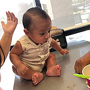 Isaiah joined the competition — help win amazing prizes! baby, child, table, indoor, window, hand, cup, spoon, sitting, curious, face, skin, clothing, person, foot, arm, daylight, background, expression, looking