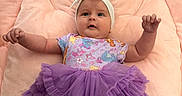 Avery is registered to the contest to win money with this photo: baby, infant, child, pink_cushion, purple_tutu, headband, onesie, toy, indoor, soft_texture, cute, lying_down, arms_raised, colorful_clothing, white_socks, carpet, happy_expression, soft_lighting, playful, portrait