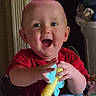 baby, child, smile, red_shirt, toy, indoor, happy, face, hands, play, infant, person, cute, joyful, bright_eyes, closeup, expression, sitting, young, cheerful