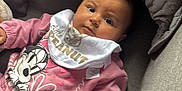 Naya is registered to the contest to win money with this photo: baby, infant, pink_clothing, bib, minnie_mouse, couch, gray_cushion, quilted_pillow, indoor, child, person, portrait, comfortable, cute, young, relaxed, casual, hand, face, expression