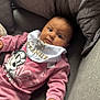baby, infant, pink_clothing, bib, minnie_mouse, couch, gray_cushion, quilted_pillow, indoor, child, person, portrait, comfortable, cute, young, relaxed, casual, hand, face, expression