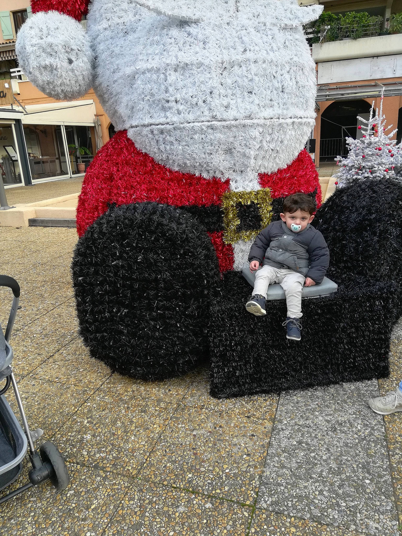 Florian participe au concours pour gagner de l'argent avec cette photo : art, bag, carmine, child, event, flooring, fur, grass, hat, lawn_ornament, luggage_and_bags, mascot, person, plant, sitting, stuffed_toy, tire, toddler, tree, winter