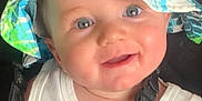 Phillip is registered to the contest to win money with this photo: baby, child, smiling, face, hat, bucket_hat, blue_eyes, white_shirt, tropical_print, car_seat, harness, straps, infant, cute, happy, portrait, indoors, seatbelt, person, closeup