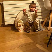 Elio participe au concours pour gagner de l'argent avec cette photo : toddler, child, indoors, chair, wooden_floor, radiator, window, happy, smiling, topknot, clothing, furniture, home, person, sitting, cute, hand_gesture, cozy, animal_print, toy