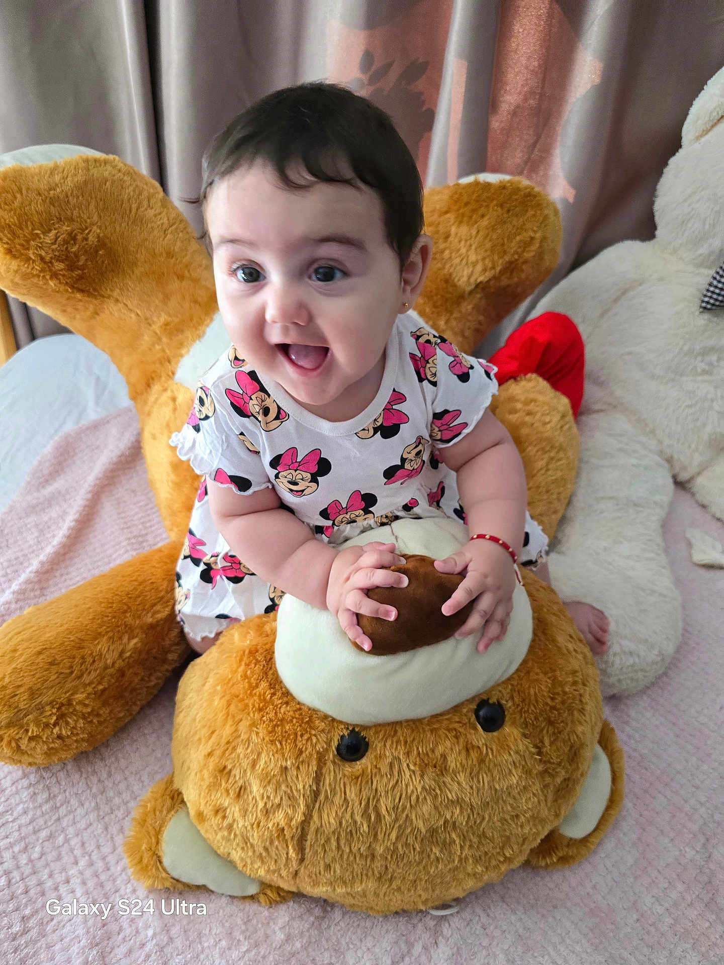 Lilianna is registered to the contest to win money with this photo: baby, child, toddler, plush_toy, teddy_bear, dress, pattern, minnie_mouse, smile, happy, indoors, bed, blanket, curtains, person, cute, soft_toy, sitting, playful, joyful