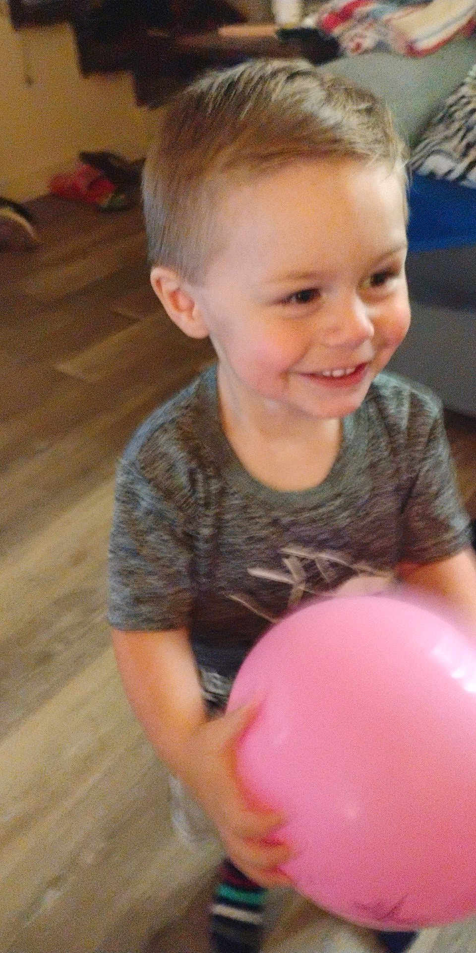 Lucas joined the competition — help win amazing prizes! child, balloon, smile, indoor, happy, toddler, short_hair, gray_shirt, wood_floor, couch, cushion, striped_socks, playful, person, home, young_child, cheerful, holding, toy, fun