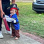 child, toddler, pirate_costume, hat, foam_sword, barefoot, outdoor, grass, sidewalk, adult_hand, smile, toy, play, costume, car, vehicle, person, fun, daylight, casual