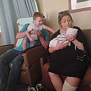 Lucas is registered to the contest to win money with this photo: adult, baby, chair, clothing, comfort, curtain, family, footwear, glasses, hand, hospital_brace, indoor, newborn, people, portrait, room, sitting, smile, toddler, woman