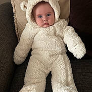 George joined the competition — help win amazing prizes! baby, child, infant, white, bear_costume, fluffy, onesie, hood, ears, blue_eyes, couch, pillow, beige, soft_texture, warm_clothing, indoors, portrait, cute, seated, cozy