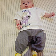 Patrick is registered to the contest to win money with this photo: baby, infant, child, lying_down, shirt, pants, socks, dinosaur_print, striped_socks, cushion, couch, barefoot, feet, indoors, cute, portrait, relaxed, comfortable, home, person