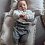 baby, infant, cushion, knit_sweater, gray_pants, socks, indoor, floor_tiles, plush, child, cute, portrait, person, cozy, casual_clothing, neutral_colors, relaxed, looking_at_camera, small_child, comfortable