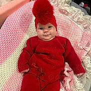 Dolcie is registered to the contest to win money with this photo: baby, blanket, bow, child, cozy, cute, hat, indoors, infant, knitted_outfit, lace, lying_down, pink, pom_pom, portrait, red_clothing, smile, soft_texture, warm_clothing, white