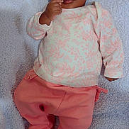 Jesulayomi is registered to the contest to win money with this photo: baby, infant, child, pink_pants, floral_top, blanket, lying_down, curious, wide_eyes, hand_near_mouth, soft_texture, indoors, cute, portrait, closeup, skin, person, cozy, sleepwear, young