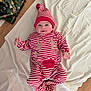 baby, infant, child, striped_clothing, red_and_white, reindeer_onesie, hat, blanket, floor, wrapped_presents, christmas_theme, smiling, cute, indoors, wooden_floor, holiday, festive, lying_down, cozy, happy