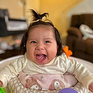 Amira joined the competition — help win amazing prizes! baby, child, infant, smiling, happy, indoor, toy, playtime, person, face, clothing, blanket, furniture, living_room, cute, portrait, sitting, hair, expression, joy