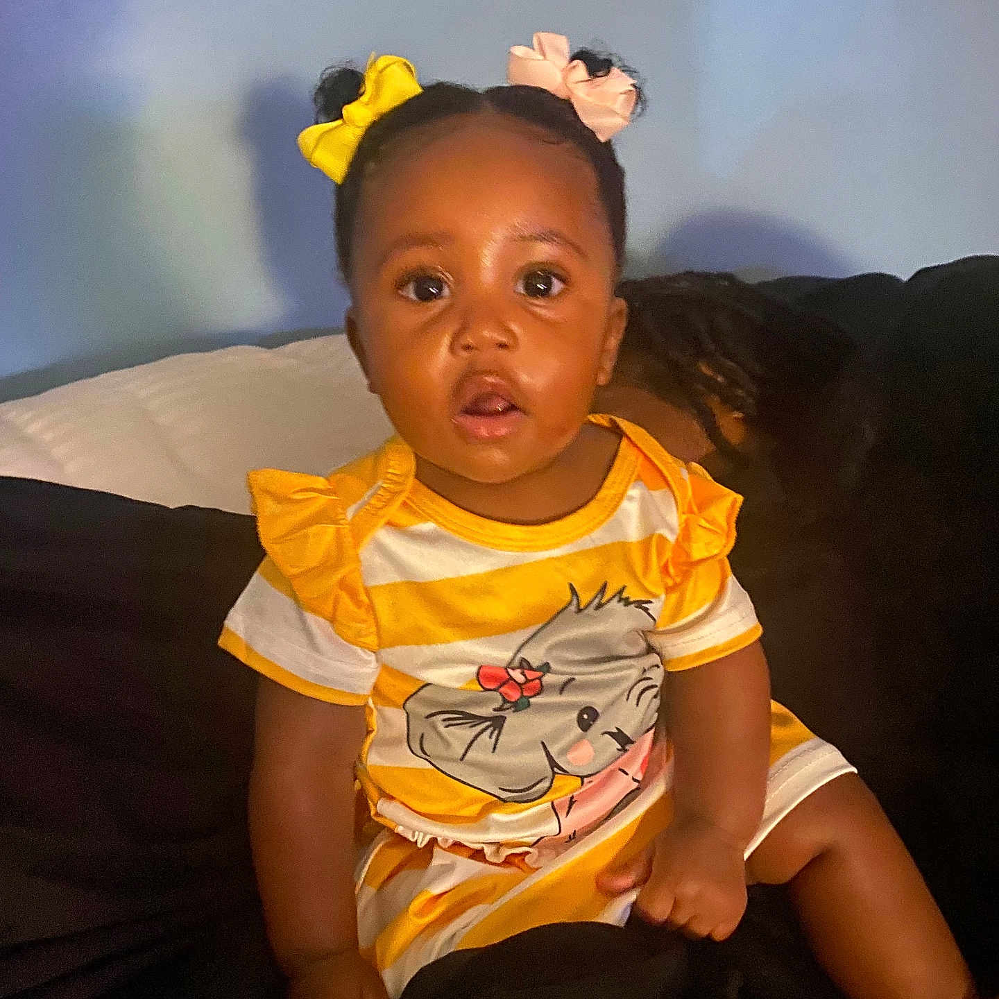 Emilyana is registered to the contest to win money with this photo: baby, black_hair, child, clothing, couch, curious, cute, dress, expression, face, girl, hair_bows, indoor, person, portrait, sitting, skin, toddler, yellow, young_child