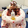 baby, infant, headband, bottle, inflatable_seat, table, snacks, indoor, person, child, clothing, pink, white, face, feet, expression, home, decor, sitting, cute