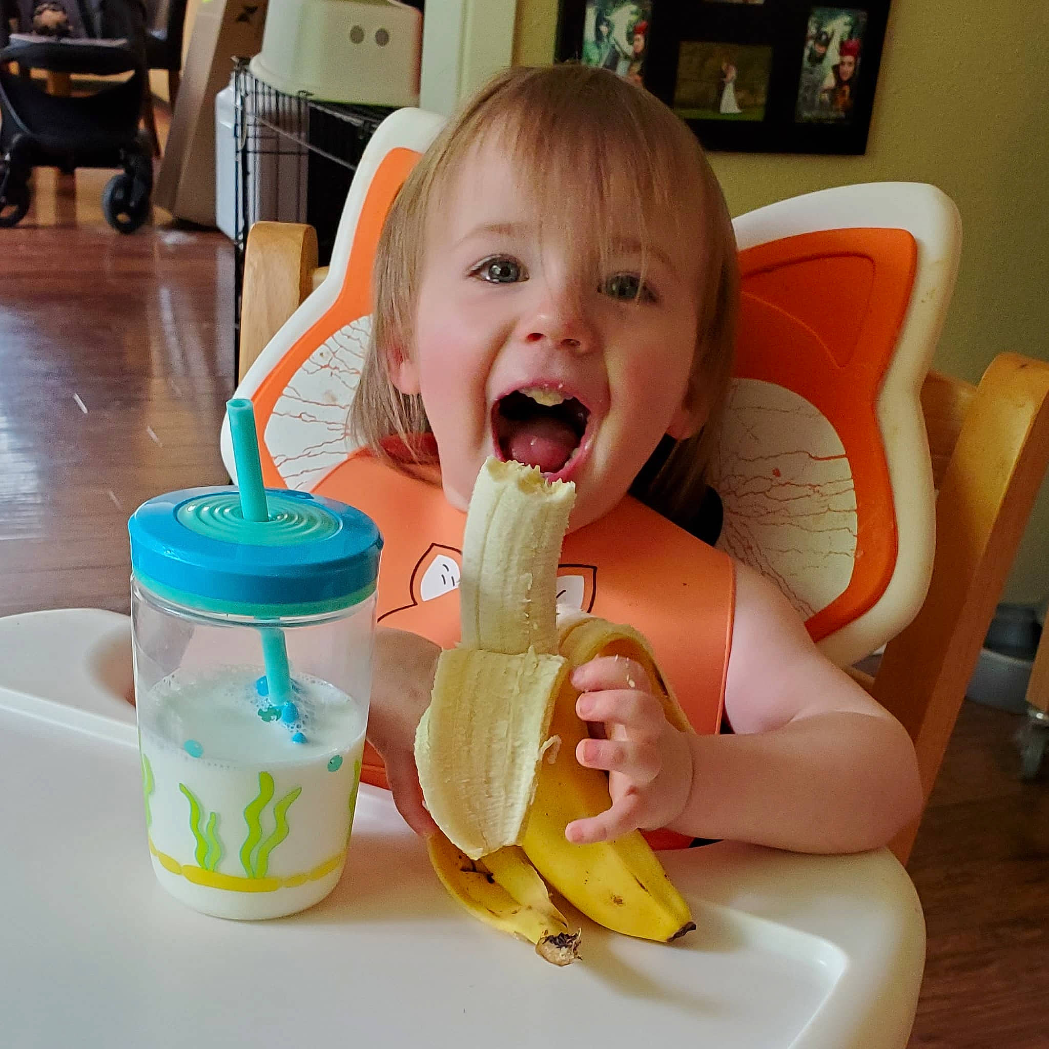 Kira joined the competition — help win amazing prizes! baby, banana, chair, child, drink, drinkware, eating, finger, food, food_craving, fruit, happy, milk, person, picture_frame, play, smile, table, tableware, television