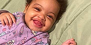 Sakura is registered to the contest to win money with this photo: baby, smiling, curly_hair, onesie, purple_clothing, space_theme, rocket, planet, lying_down, green_quilt, happy, child, infant, cute, drool, portrait, indoors, face, hand, person