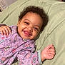 baby, smiling, curly_hair, onesie, purple_clothing, space_theme, rocket, planet, lying_down, green_quilt, happy, child, infant, cute, drool, portrait, indoors, face, hand, person