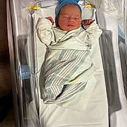 Christian is registered to the contest to win money with this photo: newborn, baby, sleeping, hospital, bassinet, blanket, blue_cap, swaddled, infant, portrait, face, closed_eyes, peaceful, medical_setting, white_clothing, tiny_hands, lying_down, nursery, birth, photography