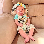 Kyler is registered to the contest to win money with this photo: baby, smile, happy, mickey_mouse, hat, clothing, infant, sitting, couch, furniture, face, person, cute, child, indoors, apparel, joy, relaxing, comfort, portrait
