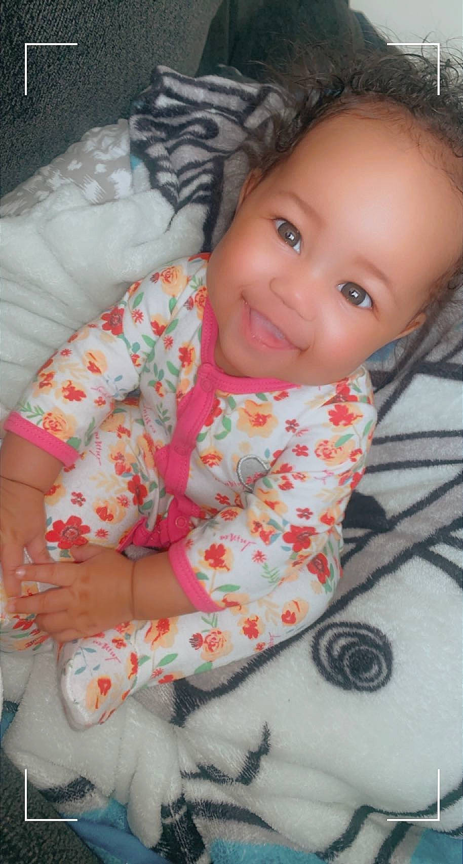 Amila is registered to the contest to win money with this photo: baby, baby_toddler_clothing, cheek, child, comfort, eye, face, happy, joy, linens, lip, mouth, nose, pattern, person, pink, sitting, skin, sleeve, smile