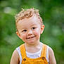 toddler, child, curly_hair, smiling, orange_overalls, white_shirt, outdoor, green_background, portrait, happy, cute, person, young_child, innocence, natural_light, close_up, face, eyes, skin, baby