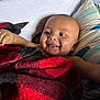 arm, baby, black, blanket, child, closeup, comfort, cozy, cute, face, happy, head, indoors, infant, lying_down, pillow, red, skin, smiling, tongue_out