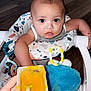 baby, baby_food, child, clothing, colorful, door, expression, face, feeding, floor, food, hand, high_chair, indoor, infant, messy, person, seat, spoon, toy
