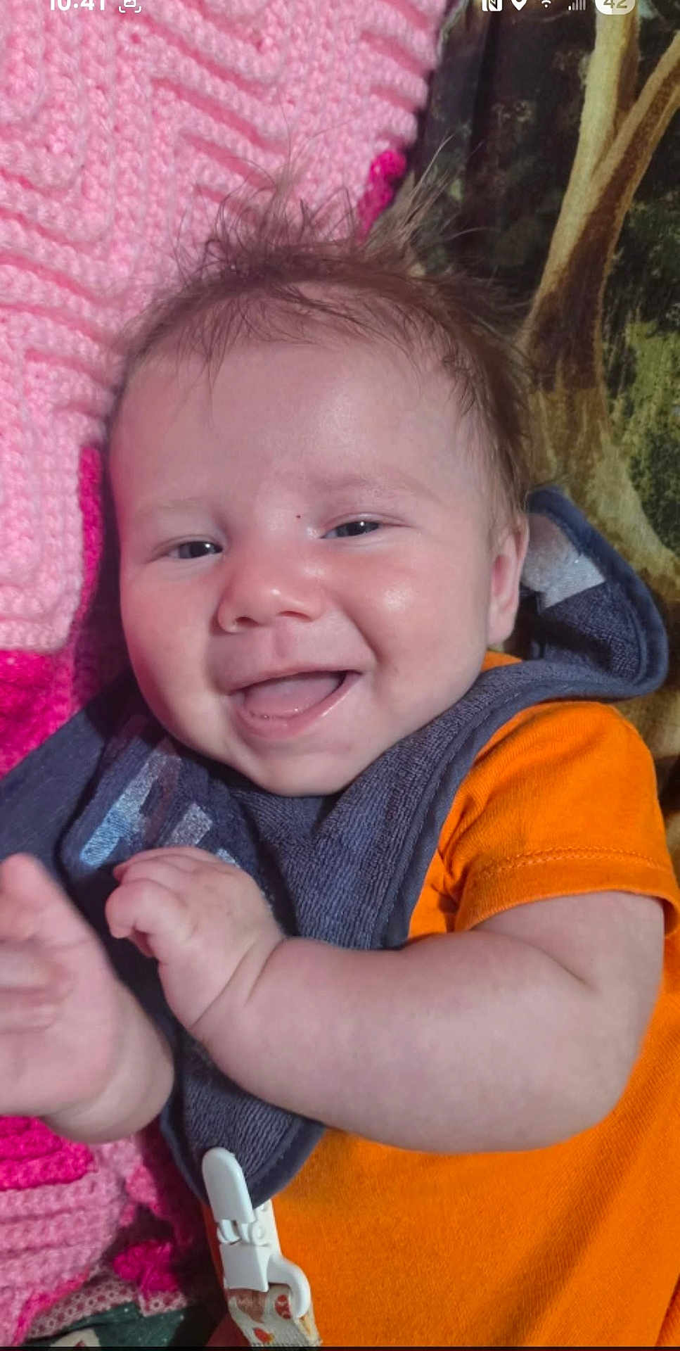 Brigham joined the competition — help win amazing prizes! baby, smiling, happy, infant, orange_shirt, bib, pink_blanket, crochet, lying_down, face, hand, skin, hair, expression, child, indoors, closeup, cute, person, portrait