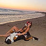 Uzzy participe au concours pour gagner de l'argent avec cette photo : dog, woman, beach, ocean, sunset, sand, shoreline, waves, outdoor, vacation, pet, animal, lying_down, playing, belly_rub, sunglasses, swimsuit, smiling, coastline, relaxation
