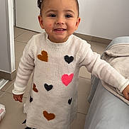 Kamila a rejoint le concours — aidez-le/la à gagner de superbes lots ! child, toddler, indoor, smiling, sweater_dress, hearts, sneakers, floor_tiles, door, blanket, couch, leaning, happy, person, portrait, casual_clothing, hair_buns, young_child, cute, playful