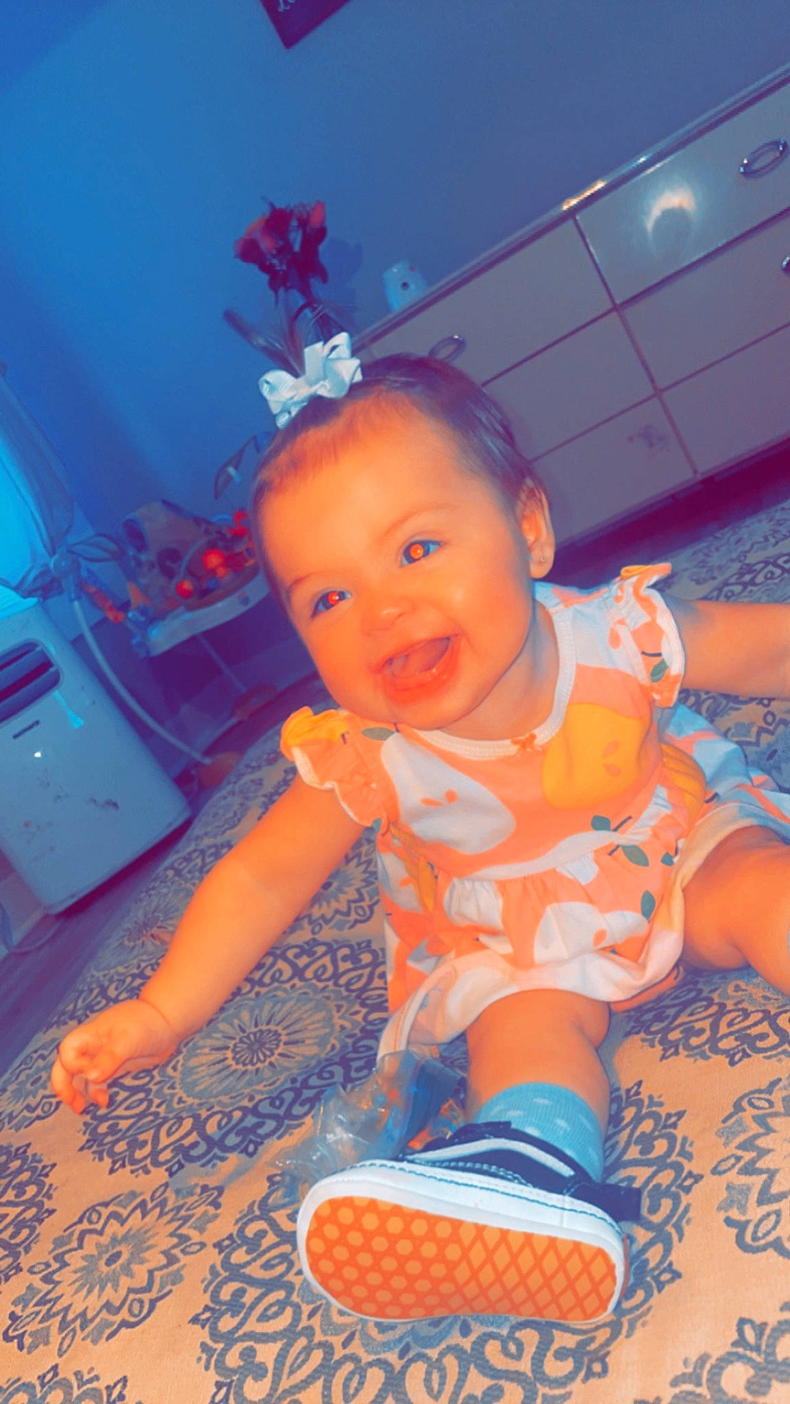 Cora is registered to the contest to win money with this photo: azure, baby, baby_toddler_clothing, blue, child, electric_blue, eye, flooring, fun, happy, houseplant, human_leg, orange, pattern, person, pink, play, sitting, smile, t_shirt