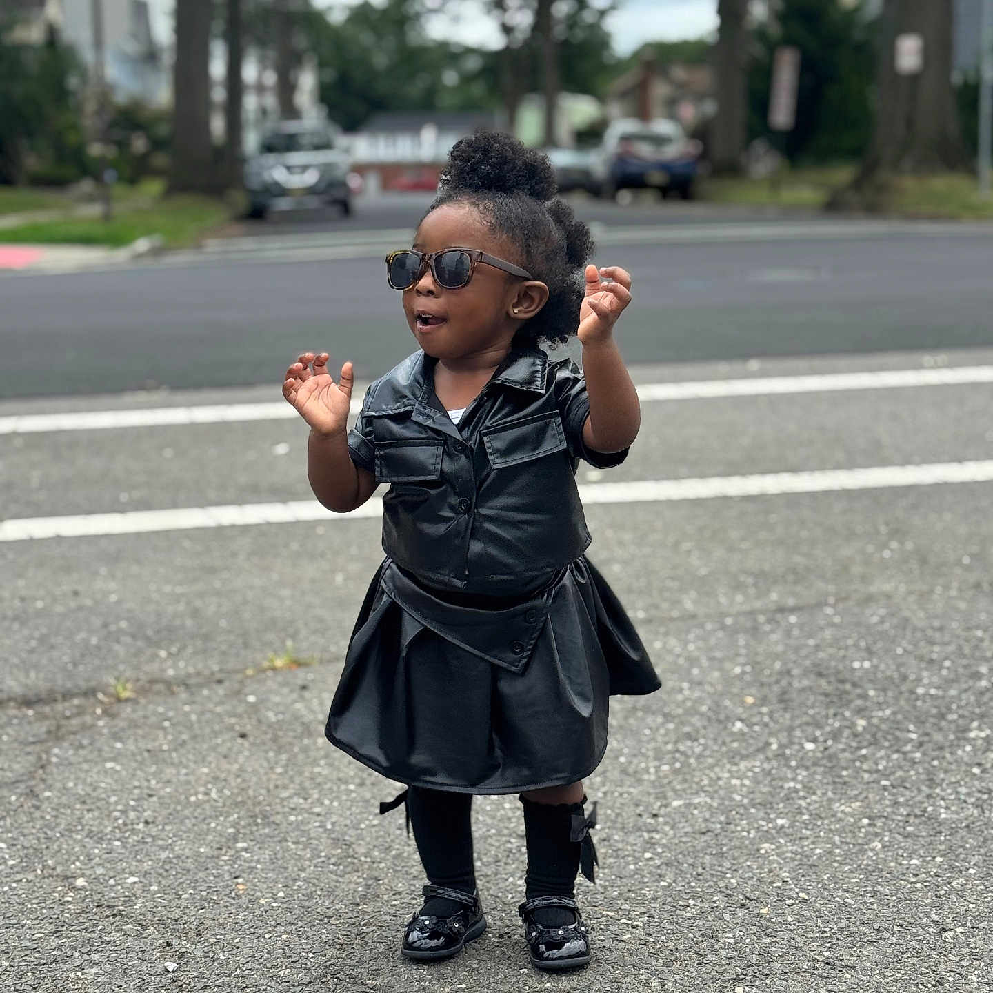 Charis is registered to the contest to win money with this photo: black_clothing, child, confident, curly_hair, daytime, fashion, hair, leather, outdoor, person, road, shoes, sidewalk, sock, standing, street, sunglasses, toddler, trees, urban