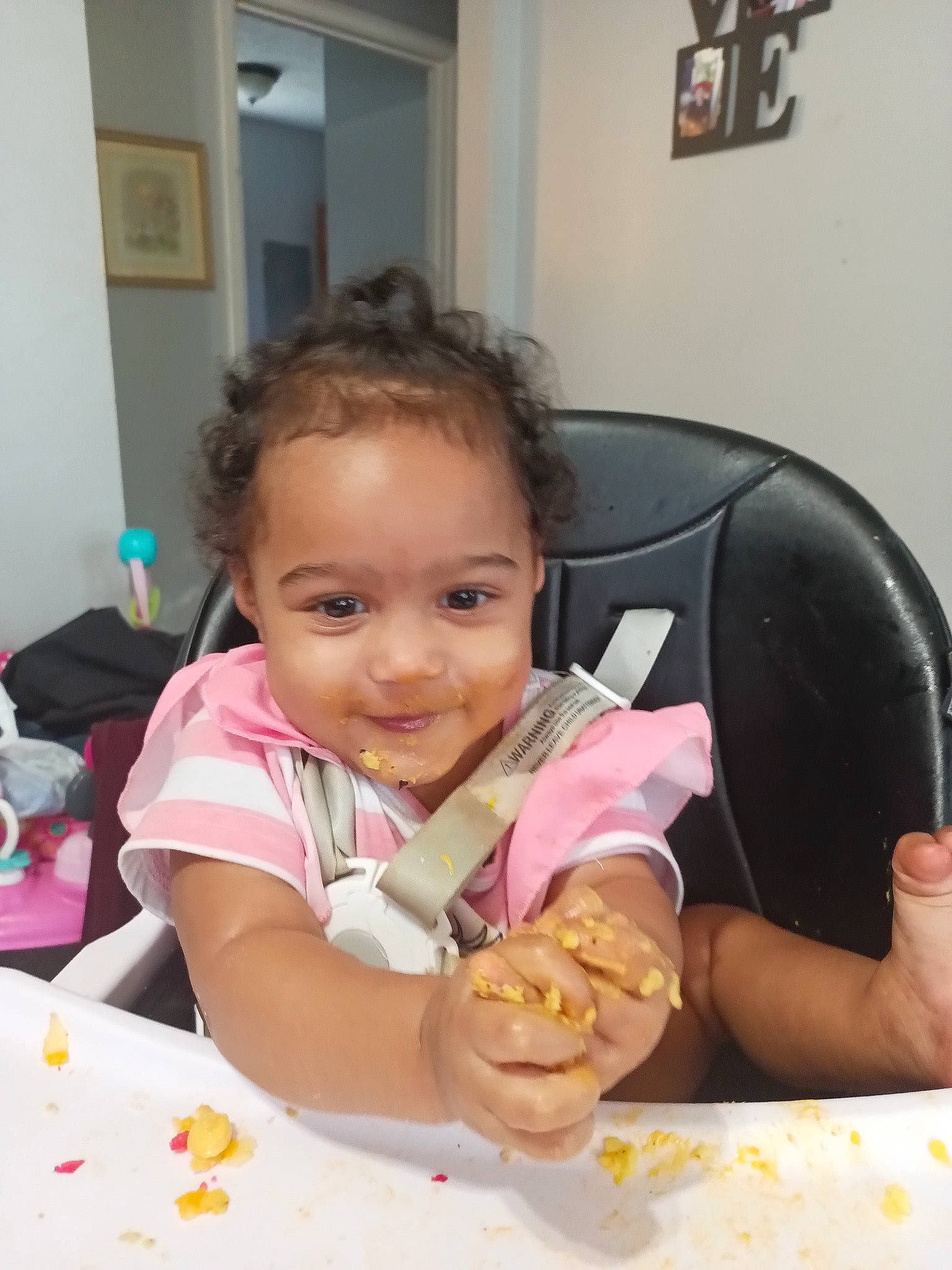 Bella is registered to the contest to win money with this photo: baby, chair, cheek, child, comfort_food, event, finger, food, fun, happy, joy, person, picture_frame, plate, sharing, skin, smile, sweetness, table, tableware