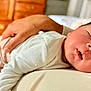 baby, sleeping, infant, hand, adult, bedroom, wooden_furniture, cozy, peaceful, rest, closeup, face, skin, clothing, white_shirt, newborn, portrait, comfort, parent, tender_moment